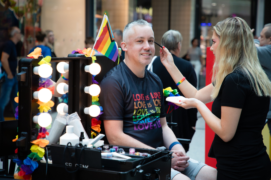 Pride 2025 Man smiling at the camera whilst a make-up artist applies glitter to his face.