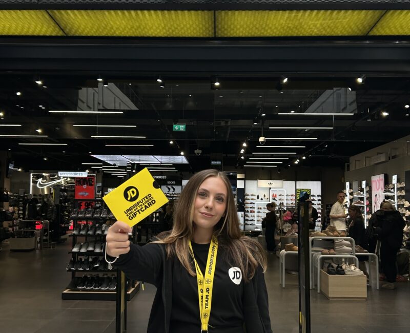 JD Sports staff member holding out a gift card at the front of their store.